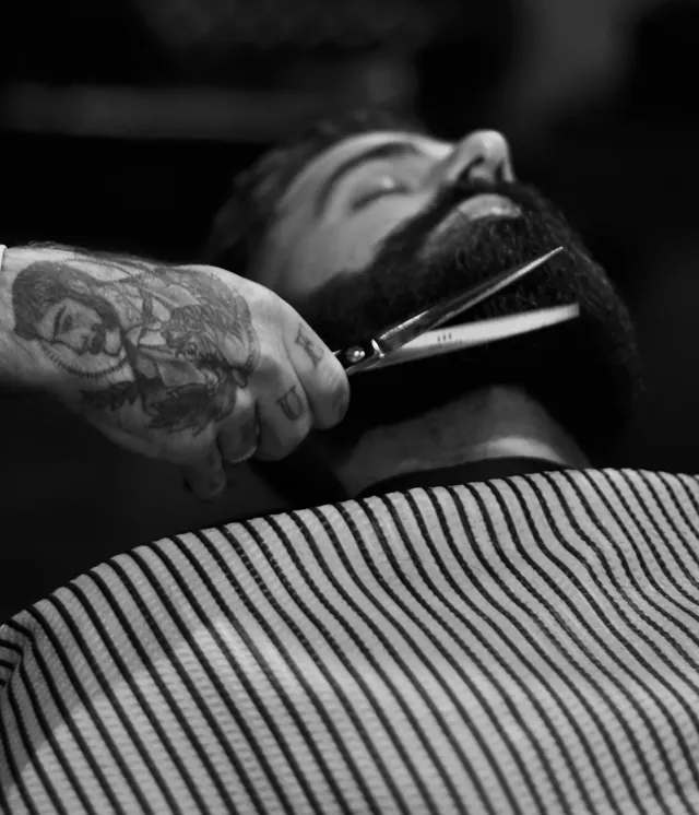 Barbiere che rifinisce la barba di un cliente con le forbici